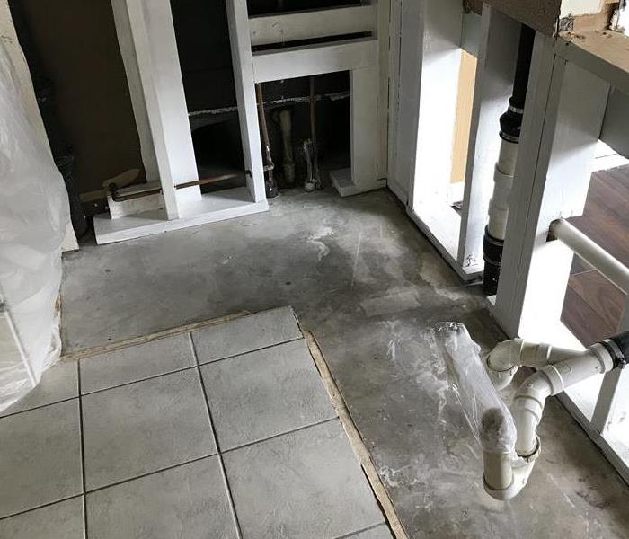 A kitchen that is being restored is being shown from the floor level. Drywall has been cut away and pipes are exposed.