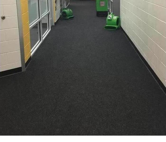 A water damaged hallway of a business is shown with SERVPRO equipment