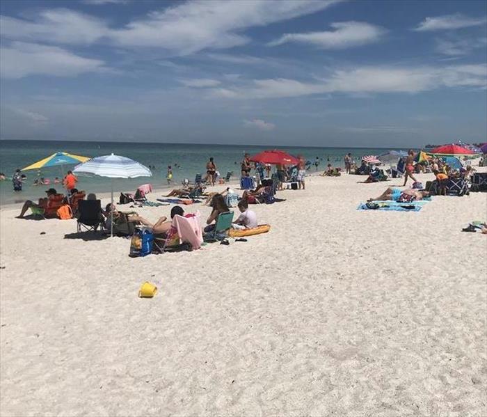 A white sand beach is shown with people and umbrellas on a sunny day
