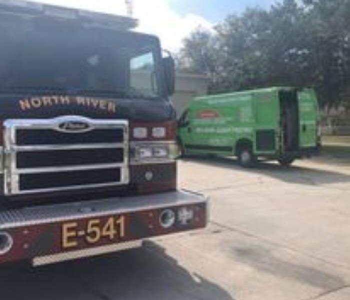 A fire truck is shown at the scene of a fire next to a green SERVPRO van