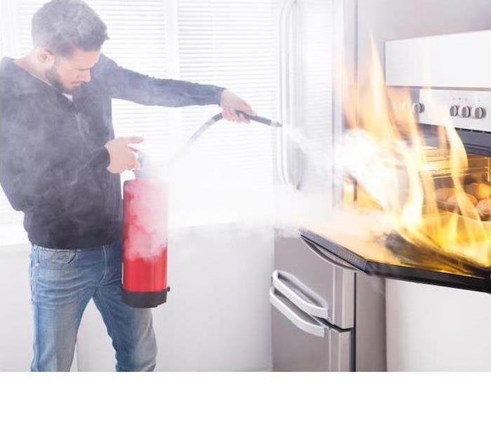 A man is shown trying to put out a kitchen fire with a fire extinguisher